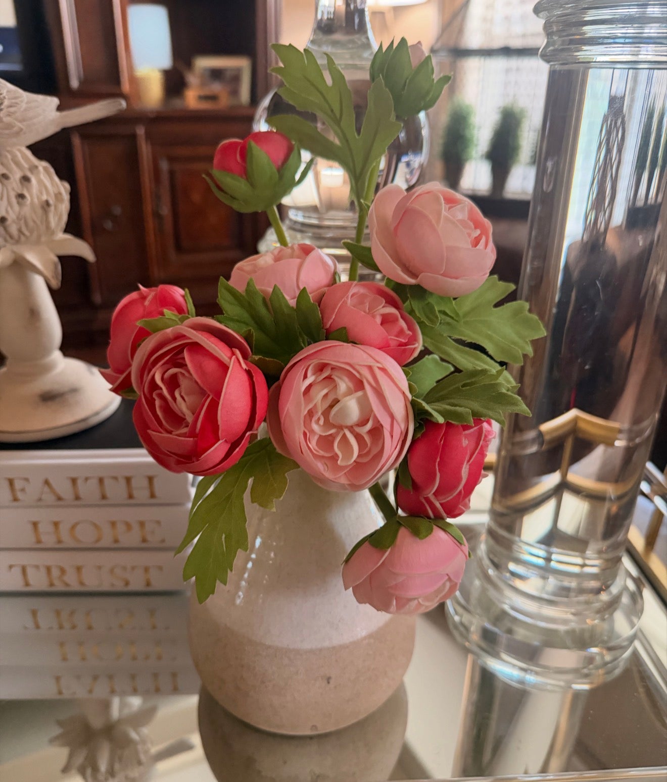 Vase with pink flowers on a reflective surface with books in the background