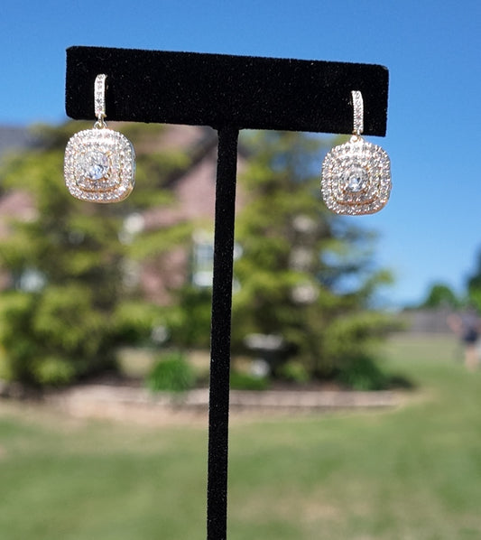 Gold crystal pavé drop earrings displayed outdoors on a jewelry stand