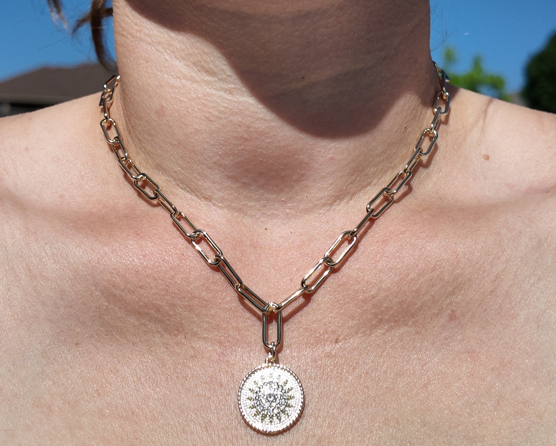 Model wearing gold sunburst medallion necklace with elongated chain links and vintage-inspired pendant