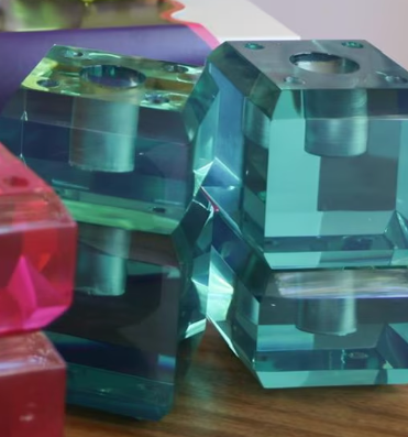Clear acrylic geometric block pieces with faceted edges and central holes, shown stacked on a wooden surface with other colored blocks partially visible. Taper Candle Holder Set