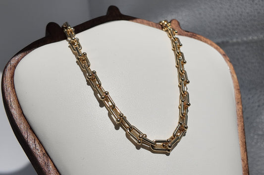 Gold Blaire paperclip chain necklace displayed on a cream jewelry stand with polished elongated link detailing