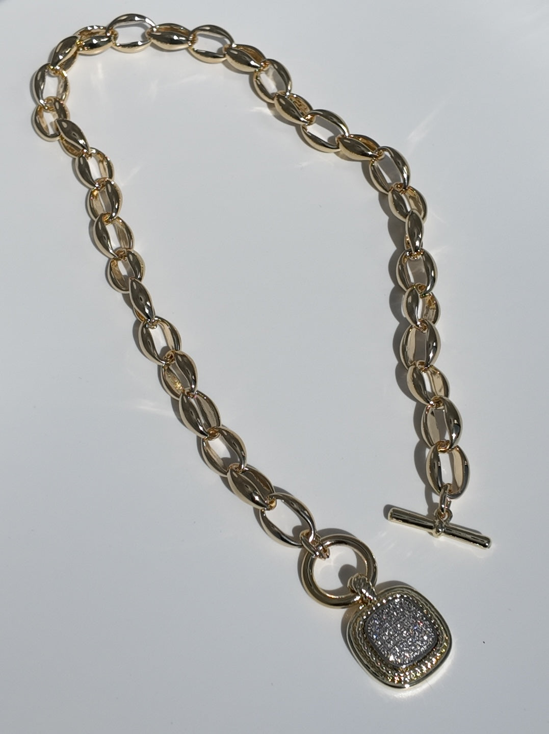 Flat lay of the Celeste Toggle Necklace showcasing elongated gold links and pavé pendant detail