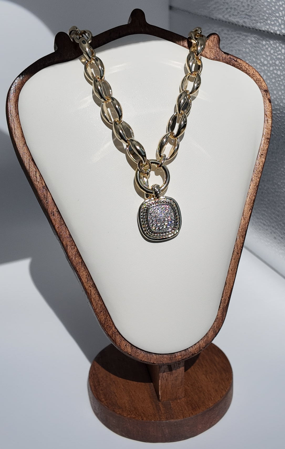 Celeste Toggle Necklace displayed on jewelry stand featuring elongated polished gold links and pavé drop pendant