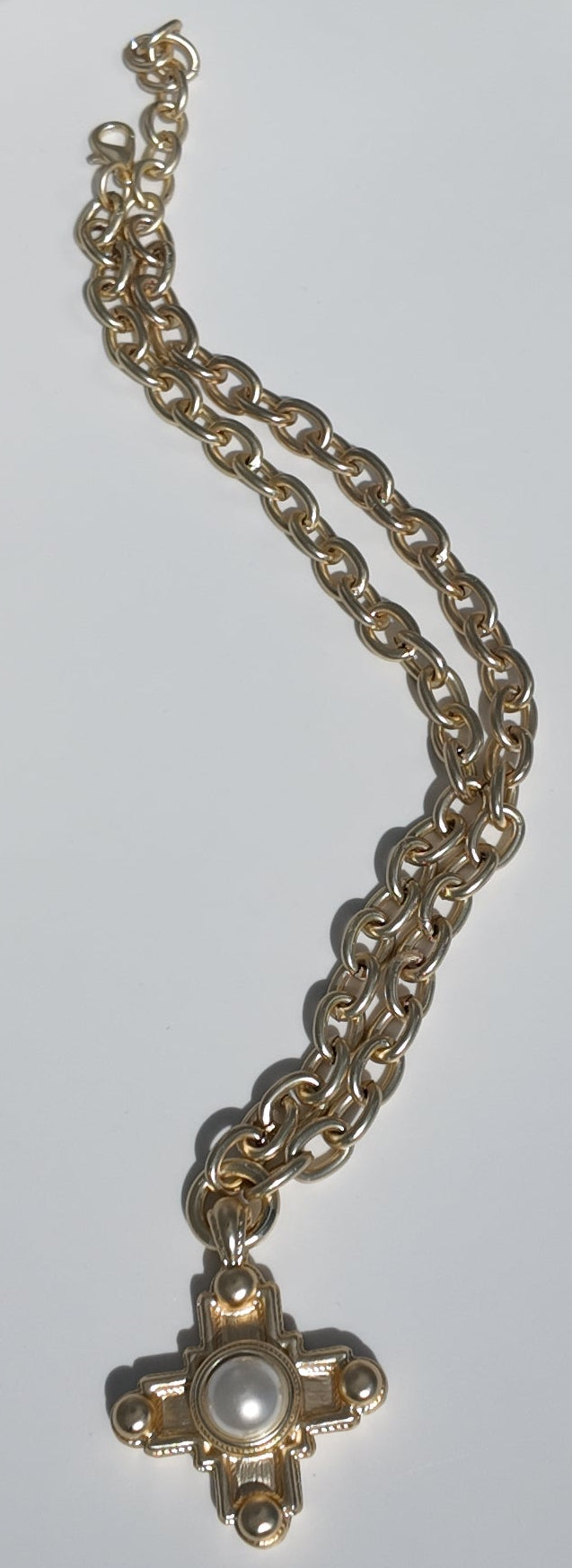 Flat lay of the Evangeline Cross Necklace showcasing matte gold chain and cross pendant
