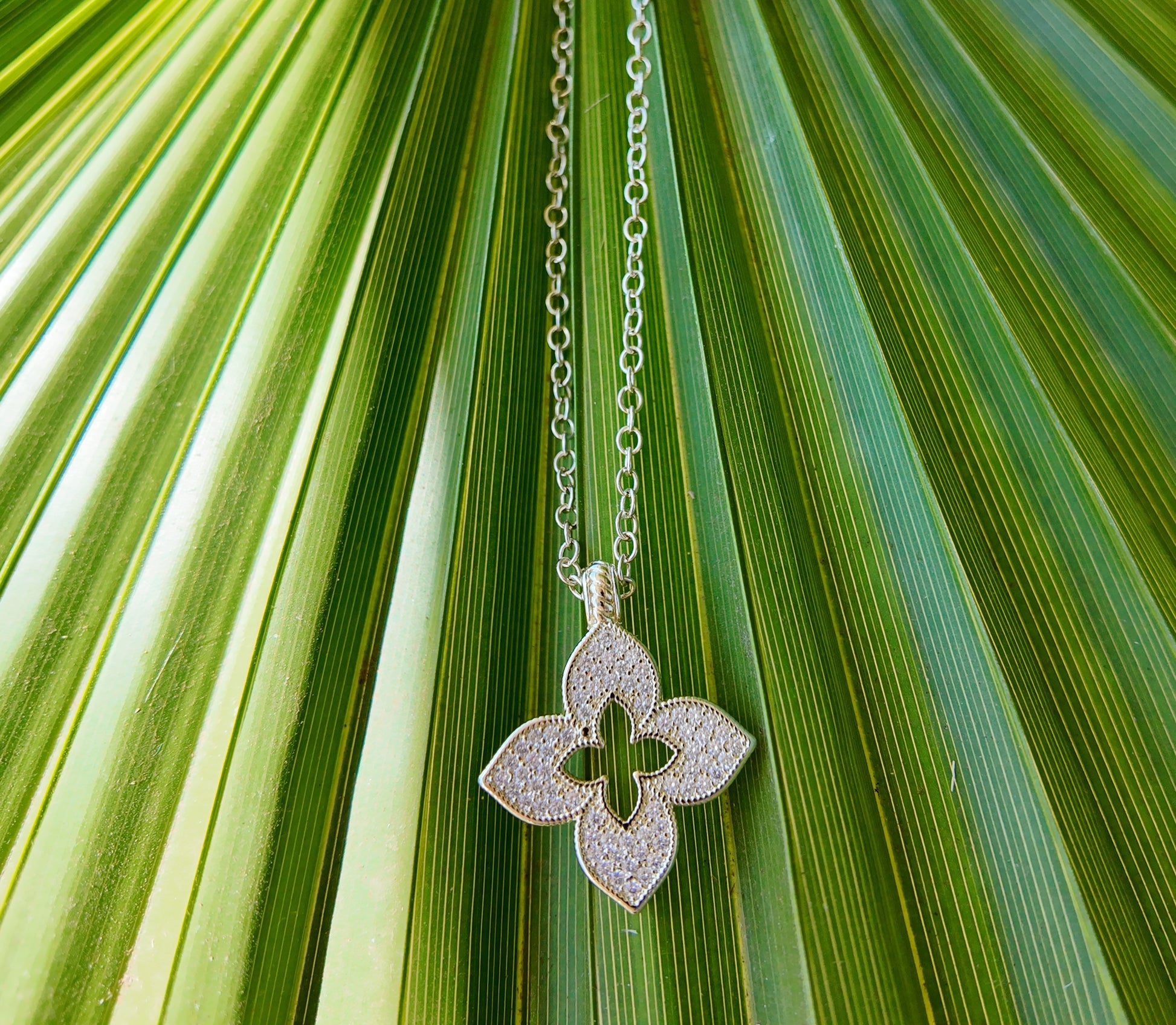 Minimalist product photo of Juliette Open Motif Necklace against textured palm leaf background