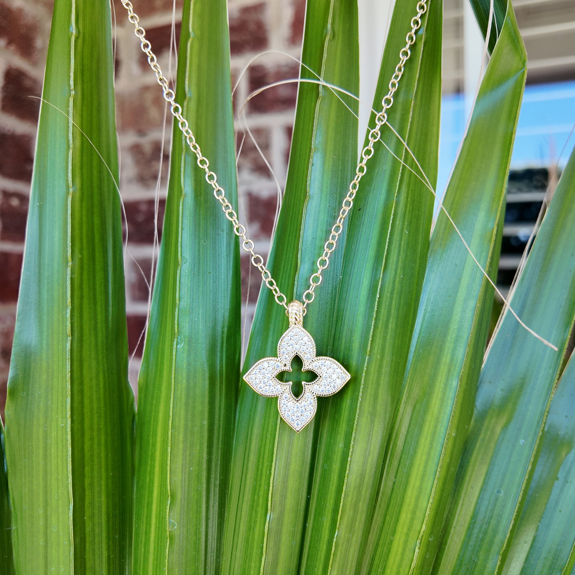Gold Juliette Open Motif Necklace photographed on tropical green palm leaves in outdoor natural lighting