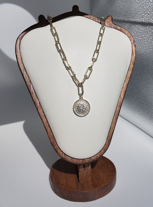 Gold sunburst medallion necklace displayed on jewelry stand with elongated chain links by Scissortail Rose Collection