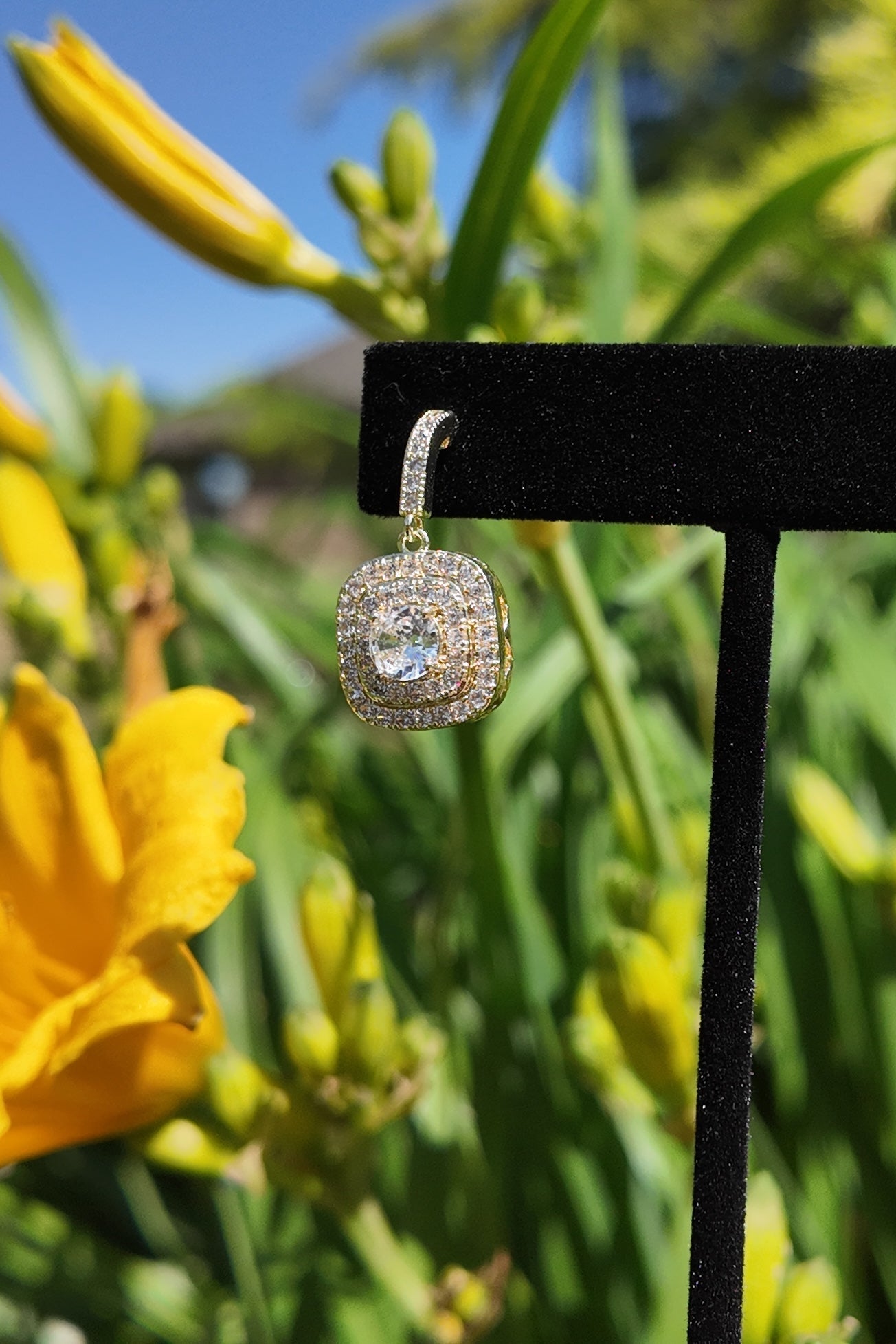 Gold pavé drop earrings displayed against a soft floral garden background