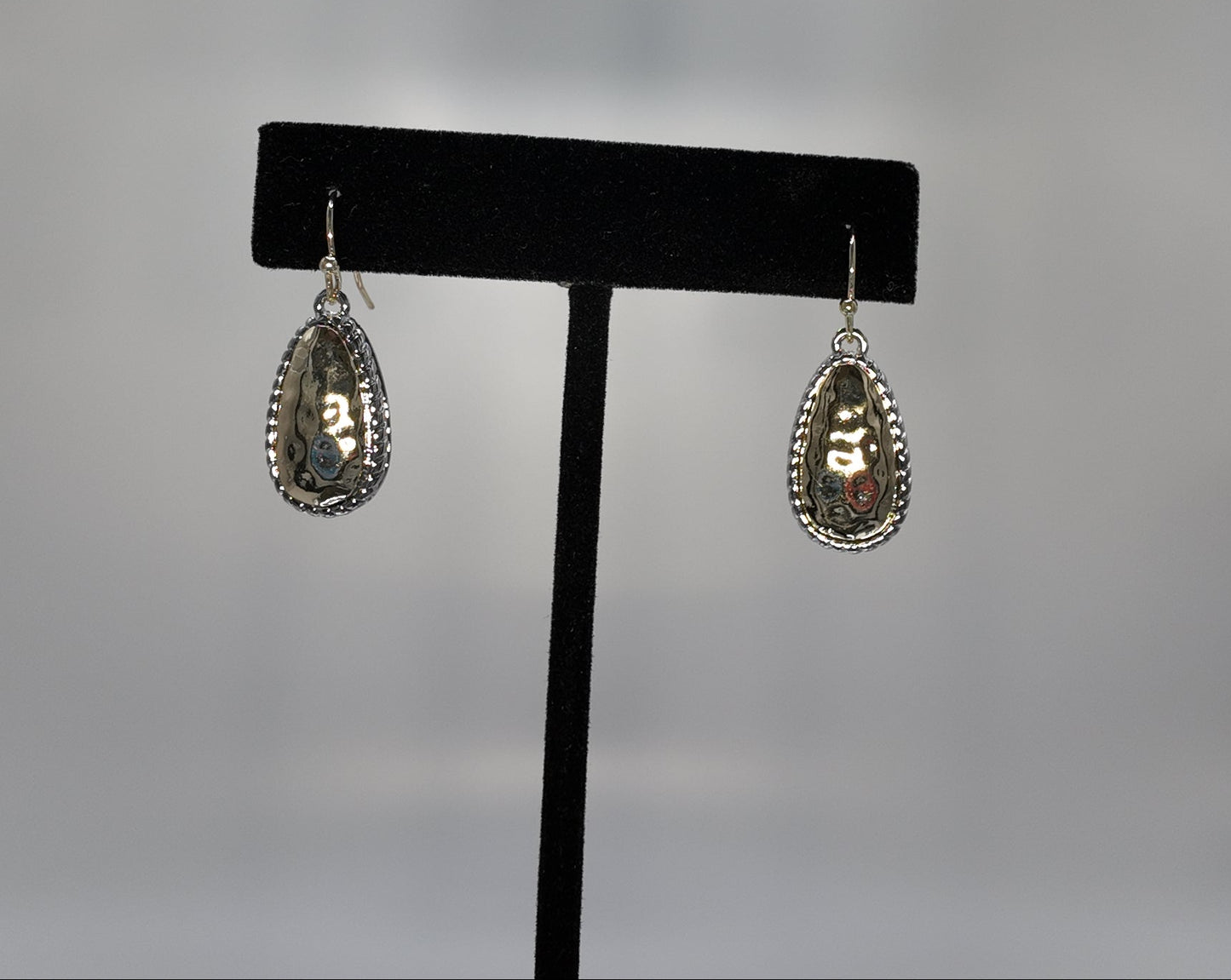 Hammered two-tone teardrop earrings displayed on a jewelry stand