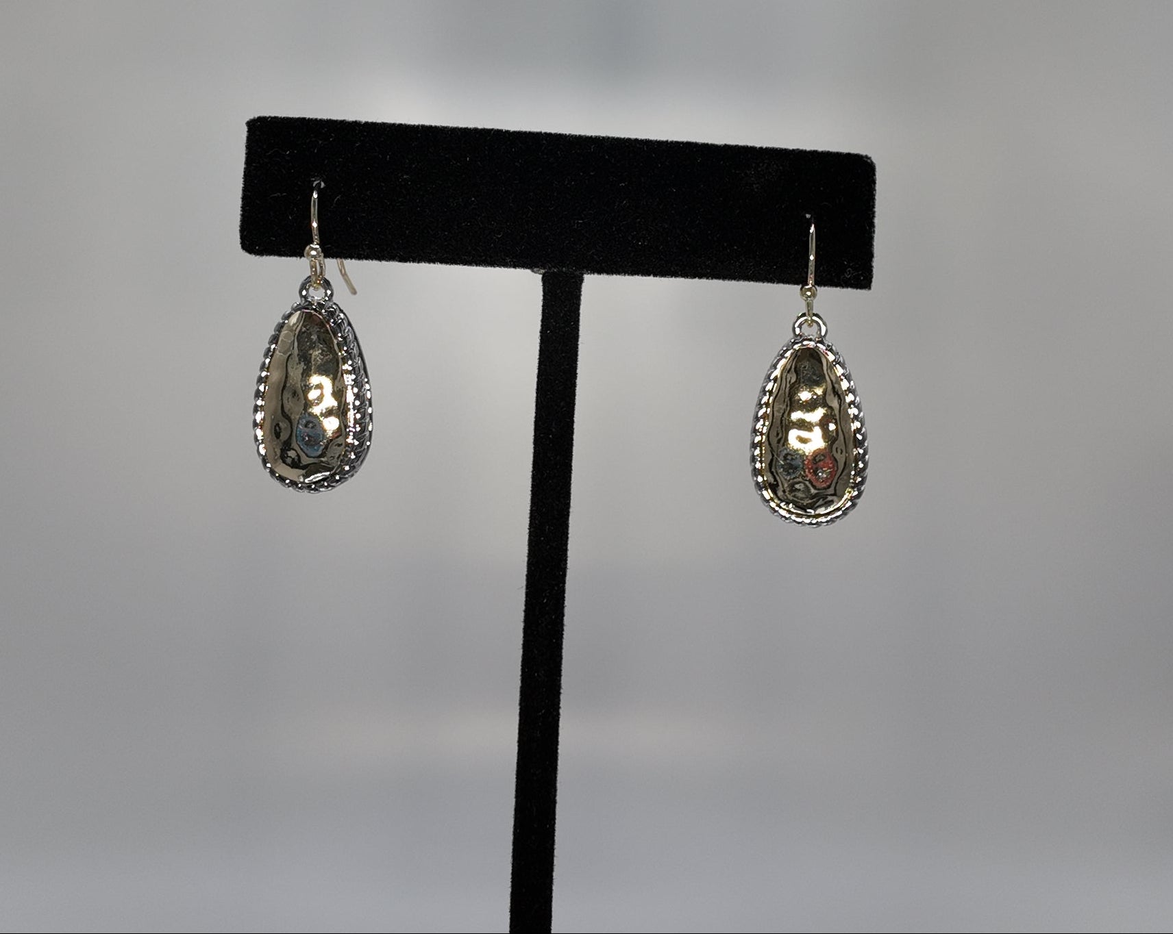 Hammered two-tone teardrop earrings displayed on a jewelry stand