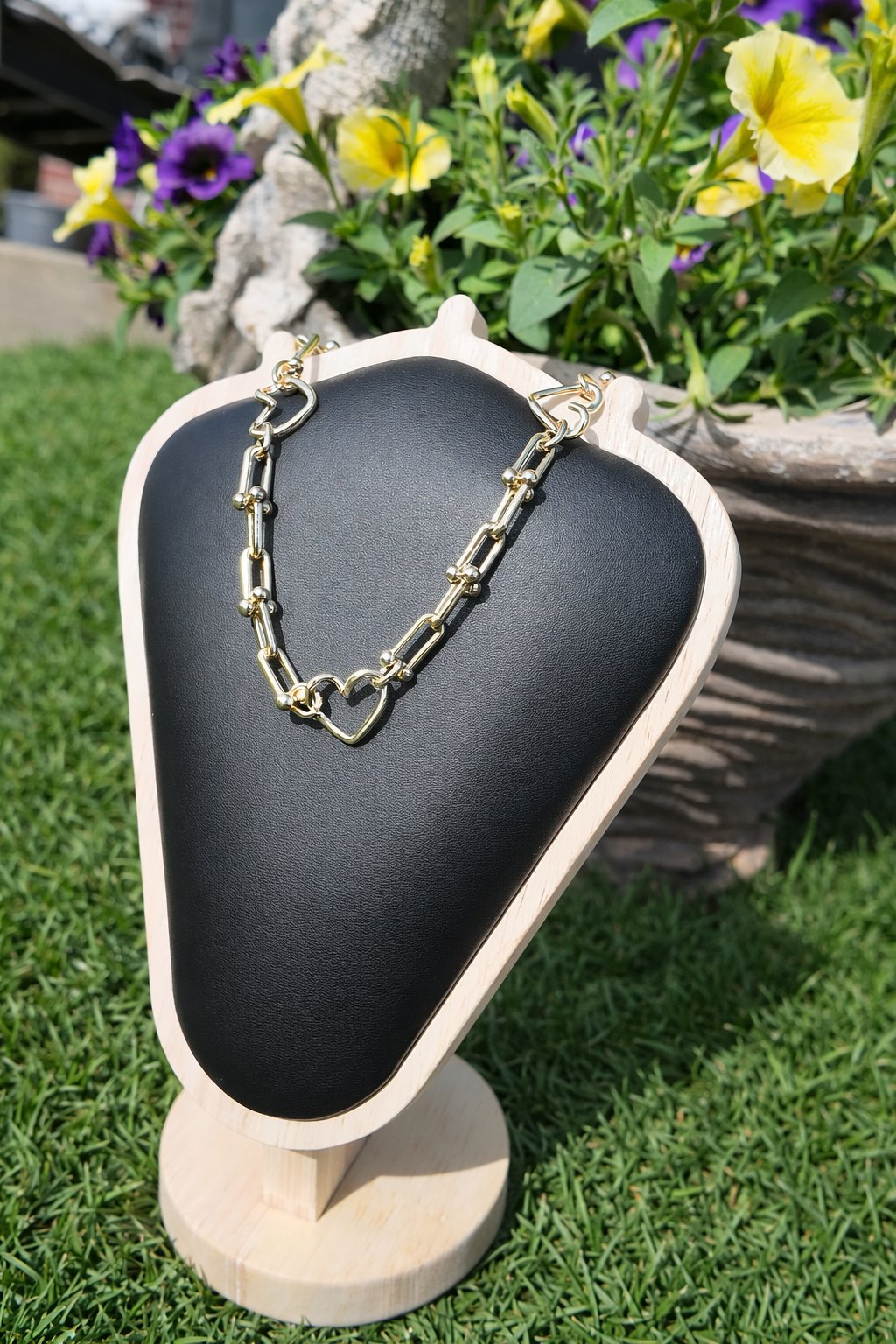 Gold heart link necklace displayed outdoors with floral background