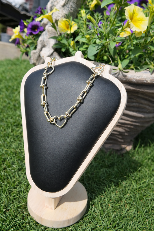 Gold heart link necklace displayed outdoors with floral background